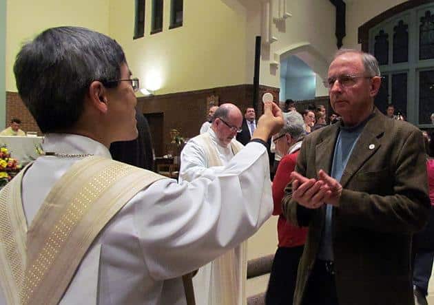 Father Ivan Tou, CSP, pastor of St. Lawrence Church and Newman Center (left), offers the Eucharist to a congregant during the parish's 125th anniversary Mass Nov. 3.