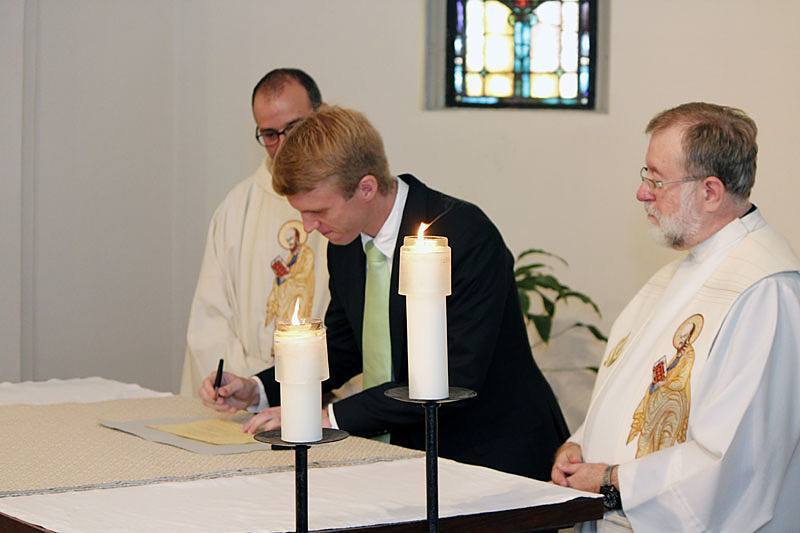 Michael Cruickshank, CSP, signs the book that lists him as a member of the Paulist community after making his first promise as Paulist President Father Eric Andrews and Paulist Novicemaster Father Rich Colgan look on.