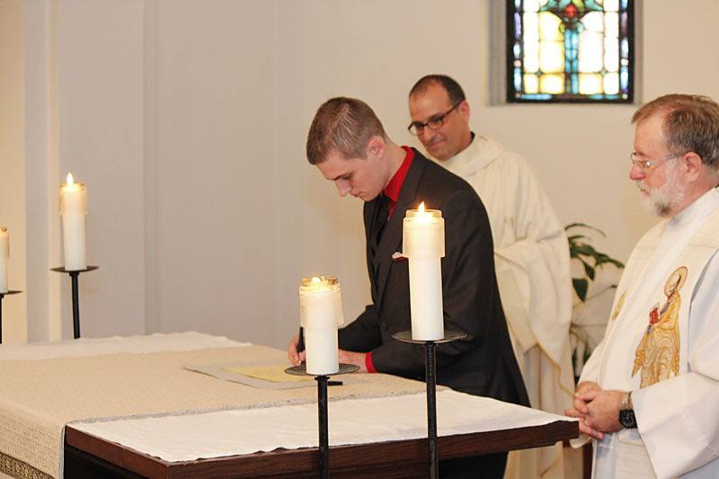 Michael Cruickshank, CSP, signs the book that lists him as a member of the Paulist community after making his first promise as Paulist President Father Eric Andrews and Paulist Novicemaster Father Rich Colgan look on.