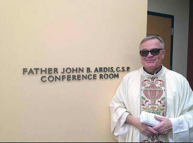 Father John Ardis, CSP, pastor of St. Paul the Apostle Church, stands by the meeting space that bears his name in the new learning center at the parish school.