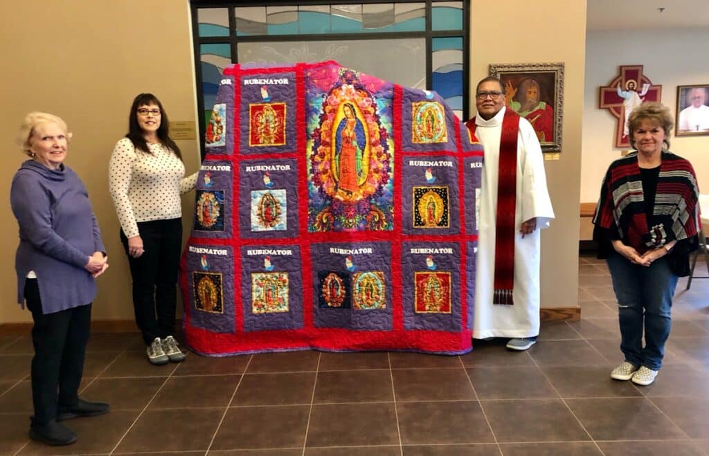 WWICS members Claudia Haydon (left), Charlie Fox (second from left) and Debbie Frazier (far right) led the project that created the “Rubenator” quilt for St. Paul the Apostle Catholic Church pastor Fr. Ruben Patino, C.S.P. (third from left). The quilt is made from “Rubenator” tee shirts St. Paul’s parishioner wore to support Fr. Ruben during his 2019 treatment for Hodkins Lymphoma. November marks the twelfth month that Fr. Ruben has been cancer free.